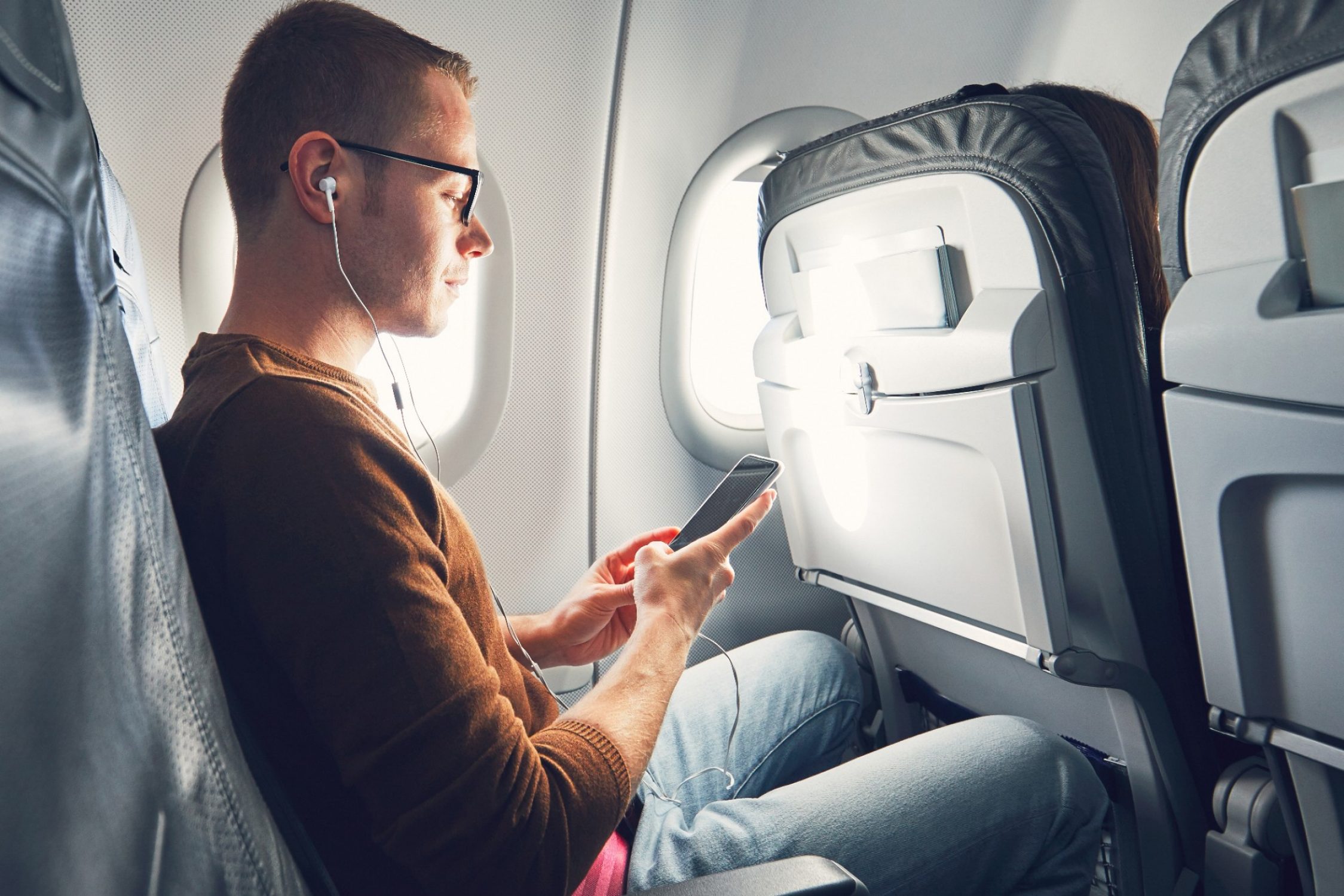 Ein Mann sitzt im Flugzeug und schaut auf sein Handy.