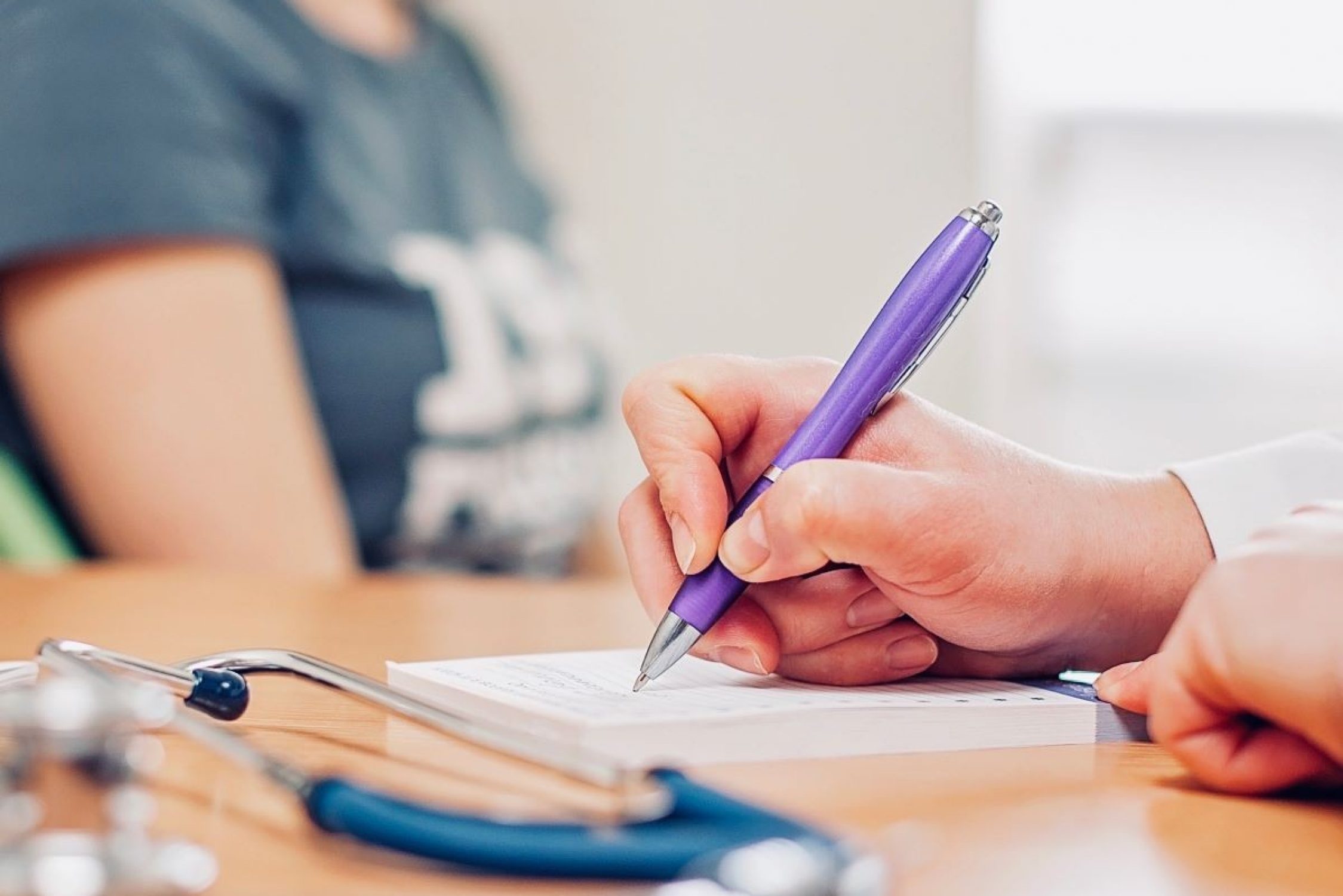 Une femme médecin écrit avec un stylo sur un bloc-notes.